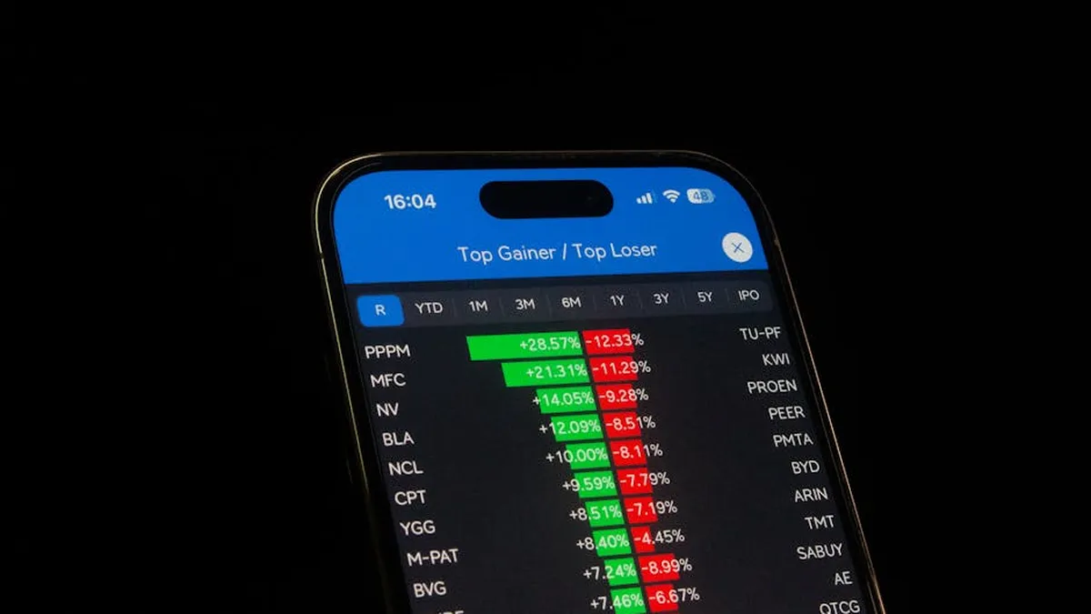 A mobile phone displaying a trading app in front of a financial market chart screen.