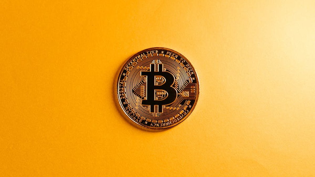 A close-up of a Bitcoin coin on a bright yellow background, symbolizing digital currency.