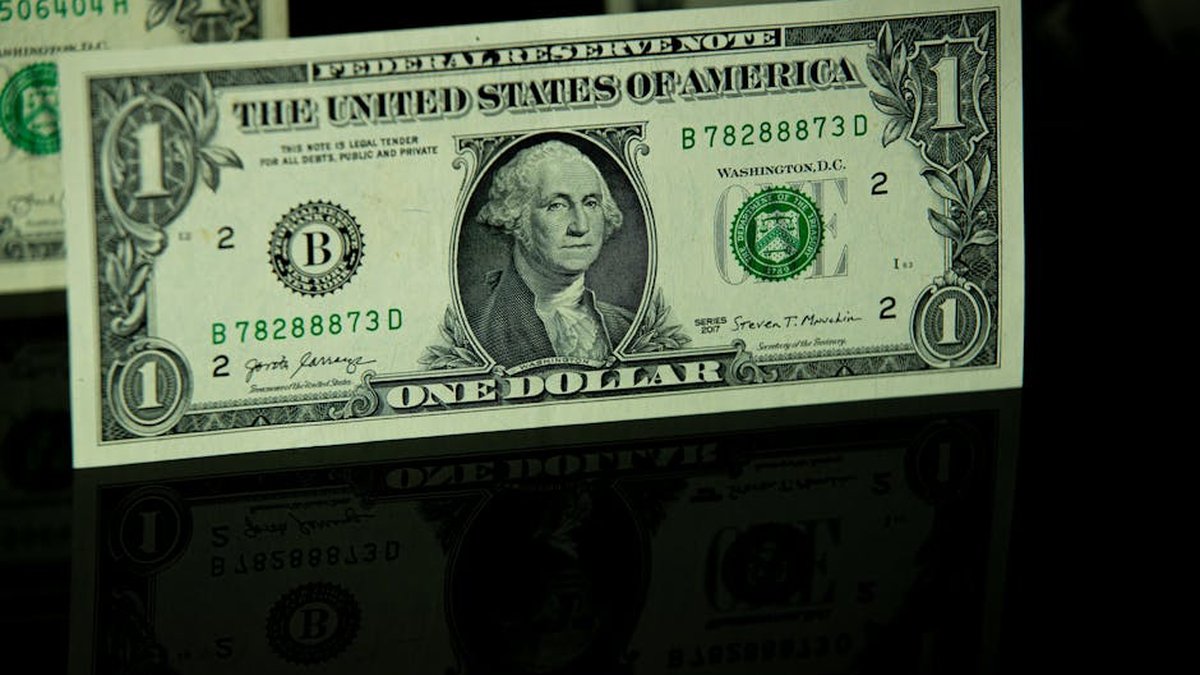 Detailed close-up of a US one-dollar bill with reflection, highlighting currency design.